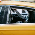 Passageira usa um smartphone sentada no banco traseiro de um táxi amarelo durante o trajeto pela cidade.