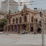 Vista do Theatro Municipal de São Paulo, cercado por arquitetura histórica e movimento de pessoas na área urbana.
