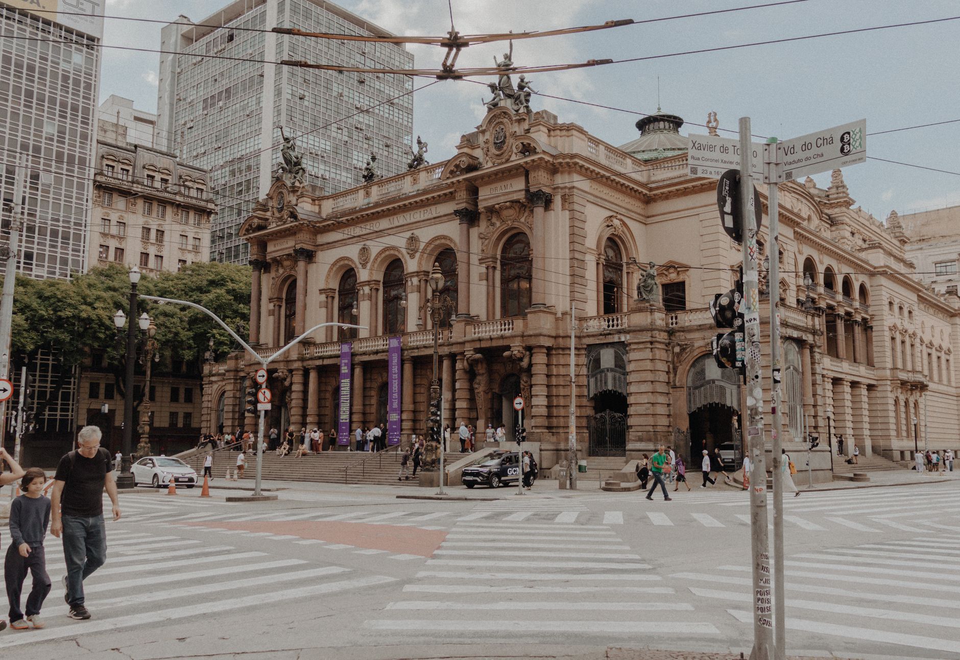 Vista do Theatro Municipal de São Paulo, cercado por arquitetura histórica e movimento de pessoas na área urbana.